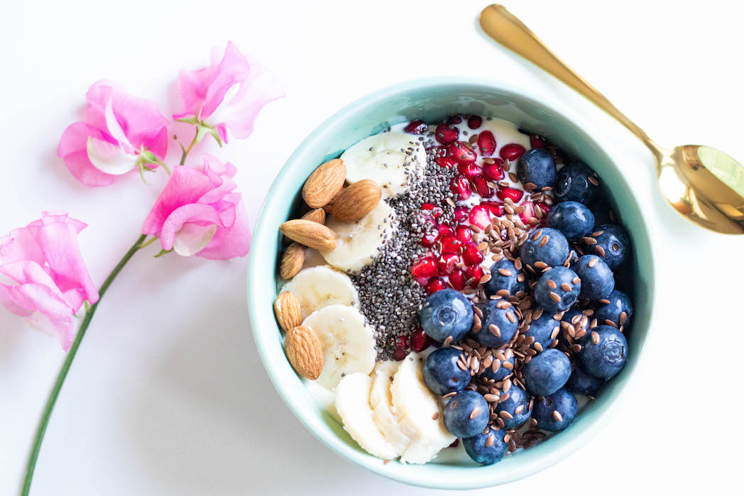 bowl with peanut butter lavender granola, almonds, banana, blueberries, pomegrante seeds, chia seeds, and flax seeds